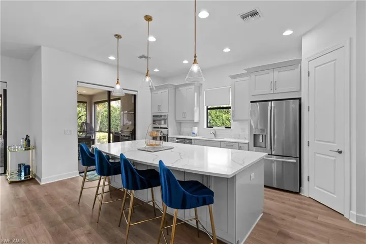 Kitchen with visible vents, a breakfast bar, wood finished floors, a kitchen island, and stainless steel refrigerator with ice dispenser