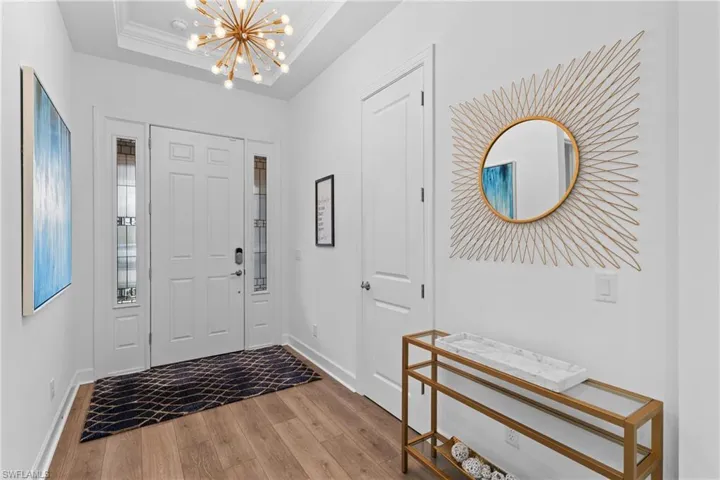 Entrance foyer with crown molding, baseboards, a chandelier, a raised ceiling, and wood finished floors