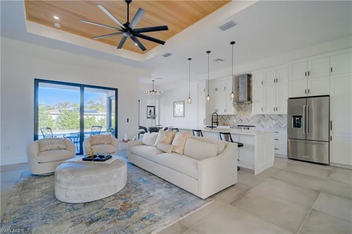 Living room featuring ceiling fan with notable chandelier, wooden ceiling, sink, and a tray ceiling