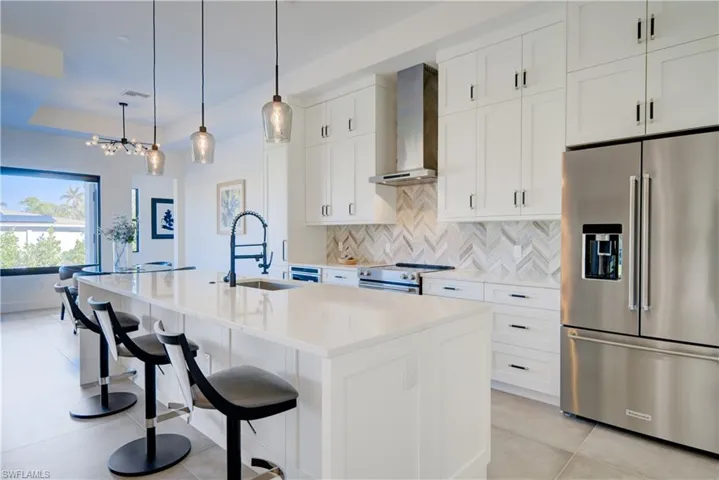 Kitchen with a breakfast bar, a center island with sink, wall chimney exhaust hood, white cabinetry, and stainless steel appliances