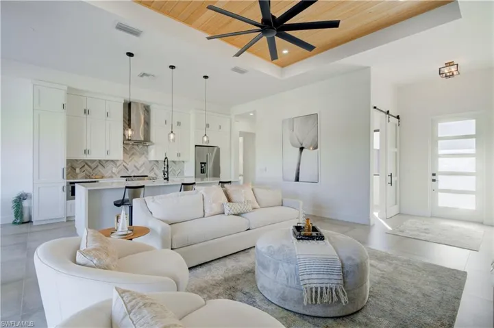 Living room with ceiling fan, sink, wooden ceiling, a barn door, and a tray ceiling
