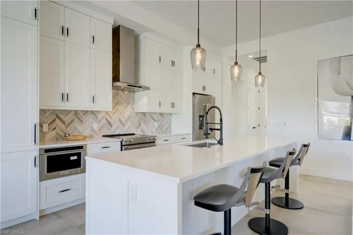 Kitchen featuring appliances with stainless steel finishes, tasteful backsplash, wall chimney exhaust hood, white cabinets, and an island with sink