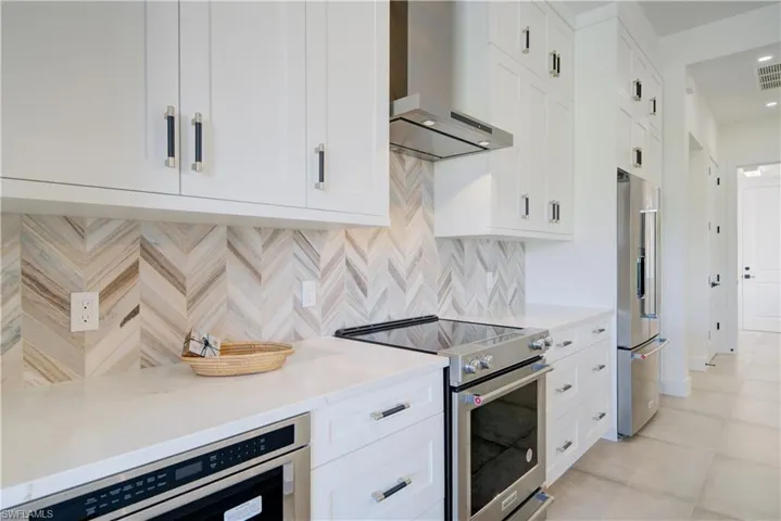Kitchen featuring white cabinetry, wall chimney range hood, and premium appliances