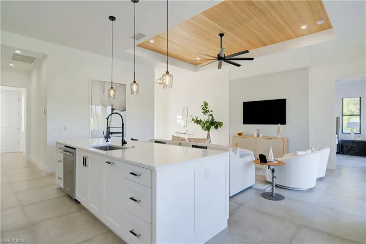 Kitchen featuring an island with sink, a raised ceiling, white cabinetry, and sink