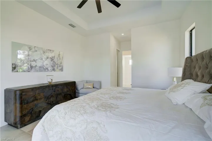Bedroom with a tray ceiling, ceiling fan, and light tile patterned flooring