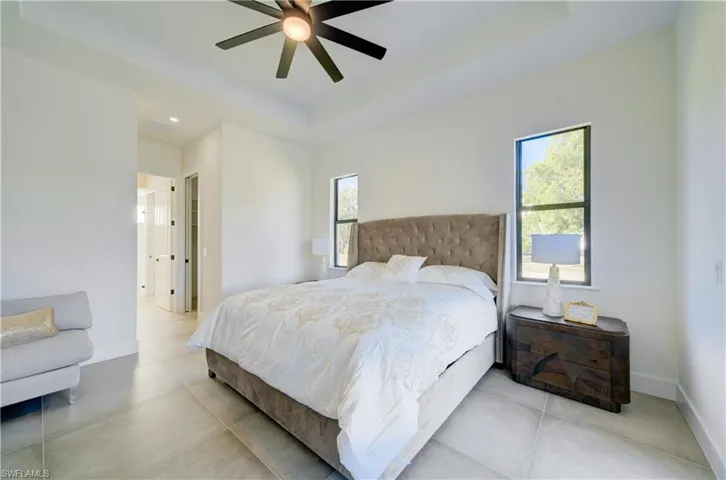Bedroom featuring a raised ceiling, multiple windows, and ceiling fan