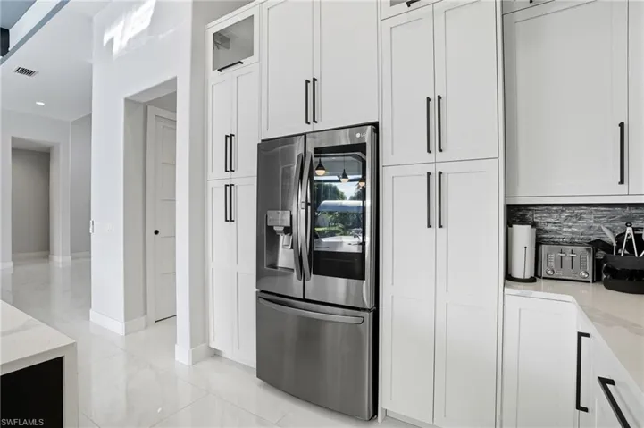 Kitchen with light stone counters, stainless steel refrigerator with ice dispenser, white cabinets, glass insert cabinets, and tasteful backsplash