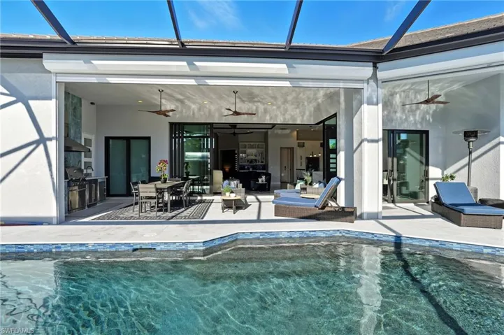 Back of house with a ceiling fan, a lanai, an outdoor pool, a patio area, and stucco siding