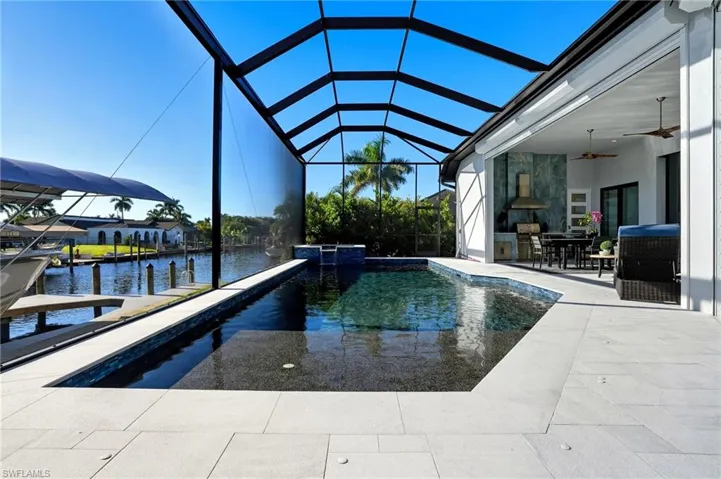 Swimming pool featuring glass enclosure, a sunroom, a ceiling fan, a patio area, and a water view