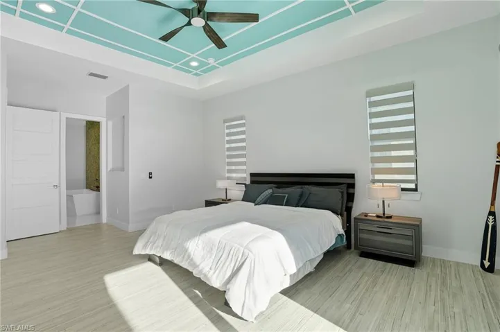 Bedroom featuring a raised ceiling, light wood-type flooring, ceiling fan, recessed lighting, and connected bathroom