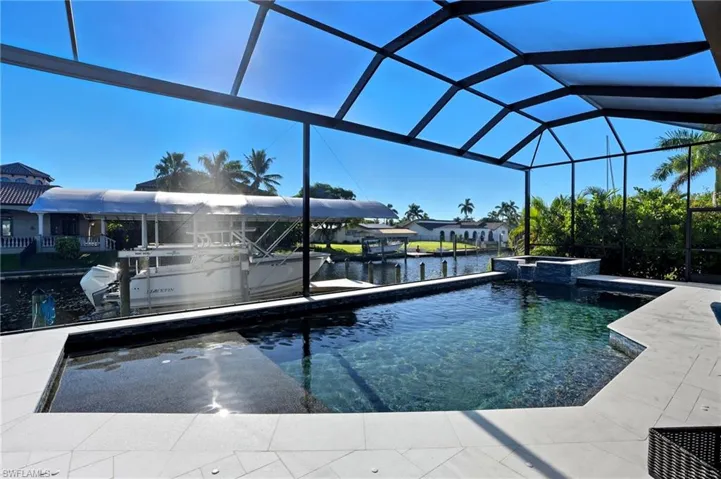 View of pool with a water view, a pool with connected hot tub, a sunroom, a dock, and glass enclosure