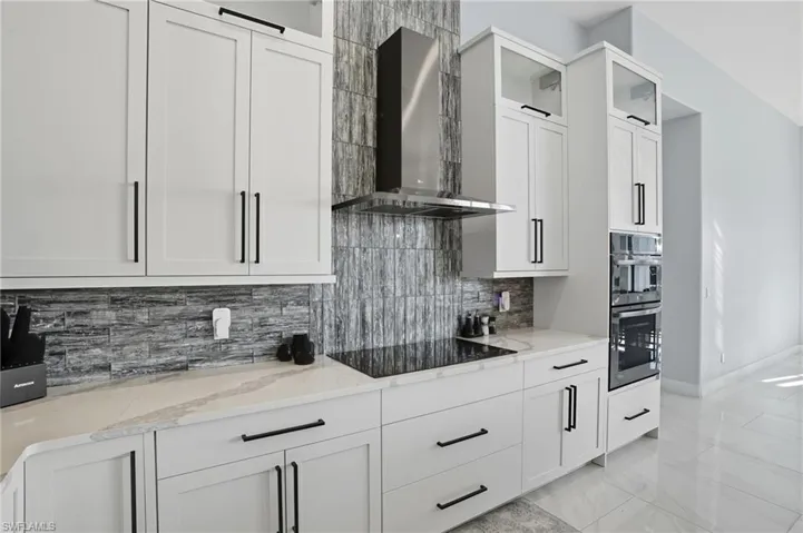 Kitchen with wall chimney range hood, white cabinetry, decorative backsplash, and light stone countertops