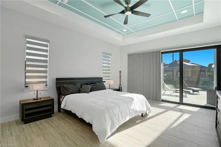 Bedroom featuring access to outside, a raised ceiling, light wood-type flooring, a ceiling fan, and recessed lighting
