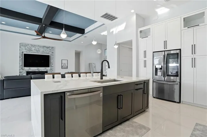 Kitchen featuring appliances with stainless steel finishes, glass insert cabinets, light stone countertops, open floor plan, and decorative light fixtures