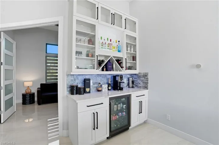 Indoor dry bar featuring white cabinetry, backsplash, glass insert cabinets, and light stone countertops