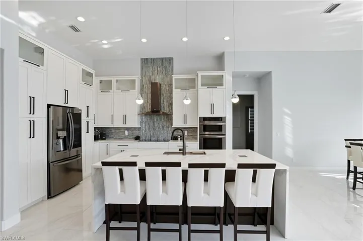 Kitchen with a kitchen breakfast bar, light stone countertops, stainless steel appliances, a center island with sink, and glass insert cabinets