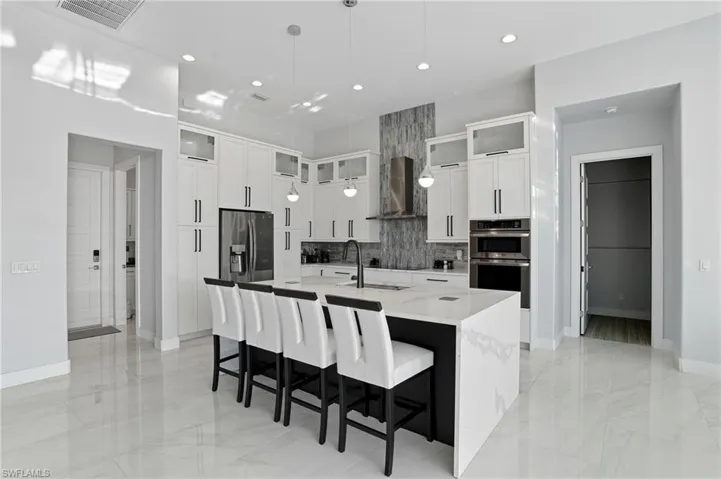 Kitchen featuring a breakfast bar area, appliances with stainless steel finishes, hanging light fixtures, white cabinetry, and wall chimney exhaust hood