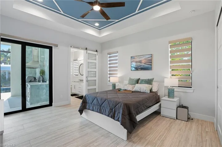 Bedroom with a barn door, light wood finished floors, a tray ceiling, a ceiling fan, and recessed lighting