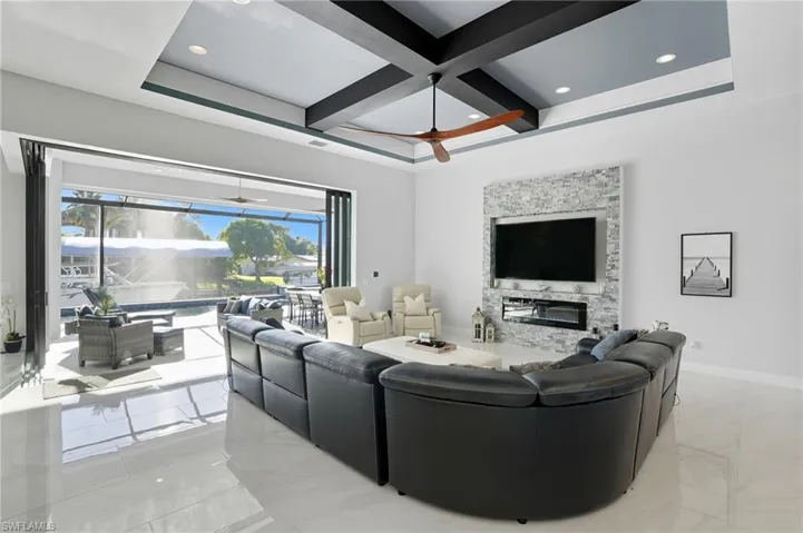 Living room featuring light marble finish floors, a glass covered fireplace, a sunroom, coffered ceiling, and ceiling fan