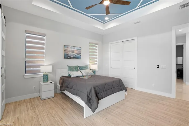 Bedroom featuring light wood-style flooring, a barn door, a ceiling fan, a tray ceiling, and recessed lighting