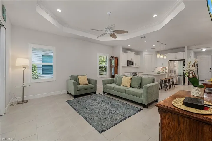 Tiled living room with crown molding, ceiling fan, plenty of natural light, and a tray ceiling