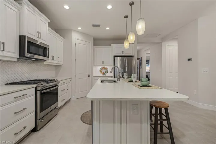 Kitchen featuring appliances with stainless steel finishes, sink, light tile patterned floors, decorative backsplash, and white cabinetry
