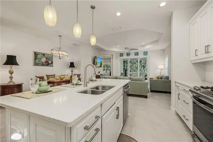 Kitchen featuring white cabinetry, an island with sink, a tray ceiling, appliances with stainless steel finishes, and sink