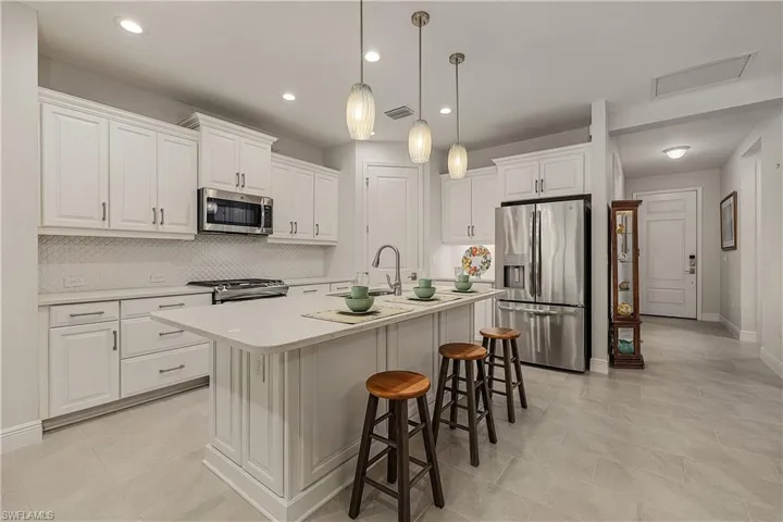 Kitchen featuring stainless steel appliances, pendant lighting, white cabinets, decorative backsplash, and a kitchen island with sink