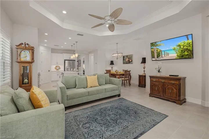 Living room with light tile patterned floors, ceiling fan, a raised ceiling, and crown molding