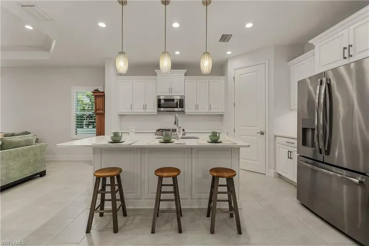 Kitchen with white cabinets, stainless steel appliances, decorative light fixtures, and a center island with sink