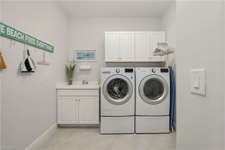 Laundry area with light tile patterned flooring, sink, cabinets, and independent washer and dryer