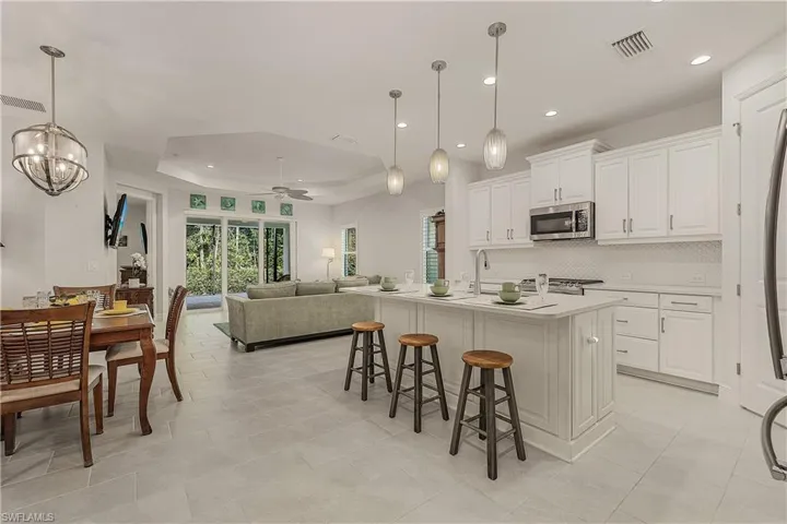 Kitchen featuring a kitchen island with sink, pendant lighting, a raised ceiling, and ceiling fan with notable chandelier