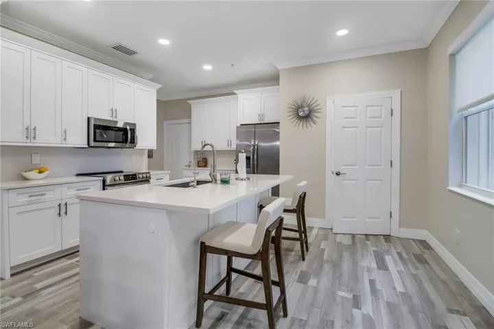 Chef's Kitchen with luxury appointments including white cabinetry, light wood-style floors, stainless steel appliances, and a center island