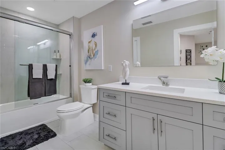 Full bathroom with vanity, tile patterned floors, toilet, and bath / shower combo with glass door