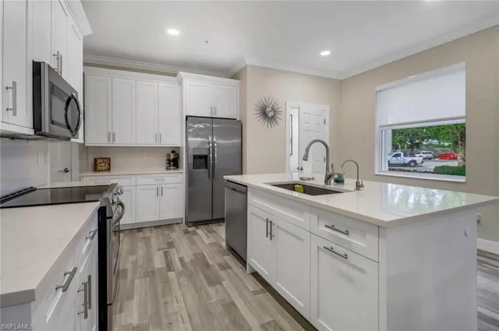 Kitchen with a spacious island, light wood-style flooring, upgraded white cabinetry, and stainless steel appliances