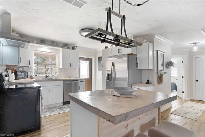 Kitchen featuring backsplash, white cabinets, sink, range hood, and stainless steel appliances