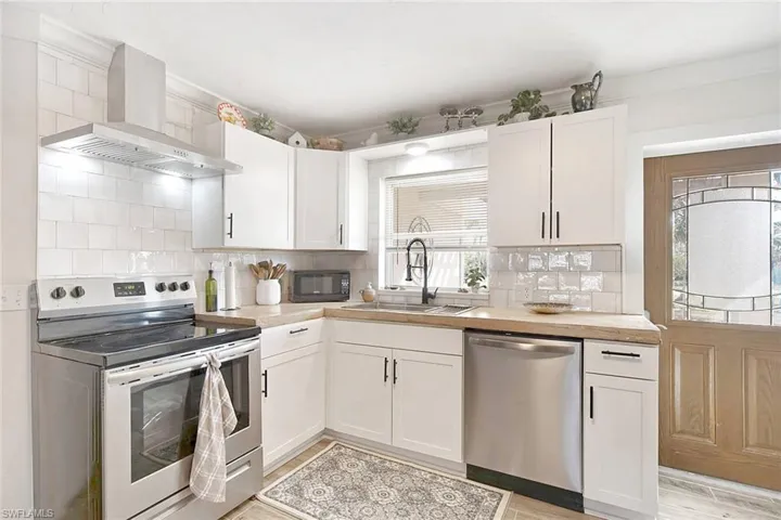 Kitchen with white cabinets, appliances with stainless steel finishes, backsplash, and wall chimney exhaust hood