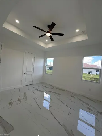 Empty room featuring a tray ceiling, light marble finish flooring, recessed lighting, and a ceiling fan