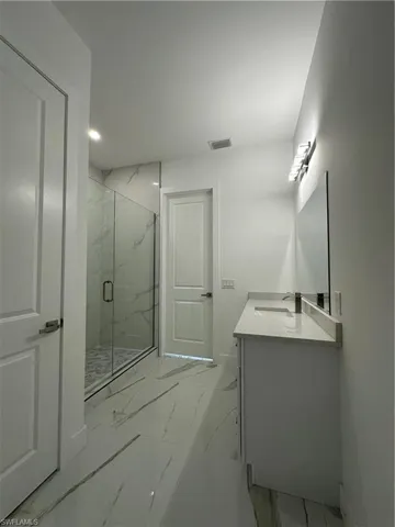 Full bathroom featuring vanity, light marble finish floors, a marble finish shower, and recessed lighting
