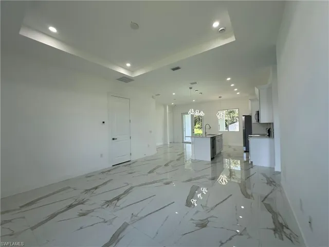 Unfurnished living room featuring light marble finish floors, a raised ceiling, and recessed lighting