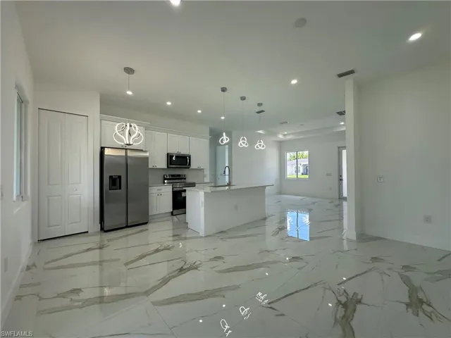 Kitchen with stainless steel appliances, white cabinetry, light marble finish floors, open floor plan, and hanging light fixtures