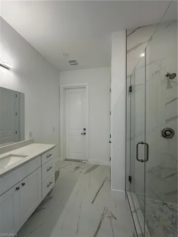 Bathroom featuring a marble finish shower, vanity, and light marble finish flooring