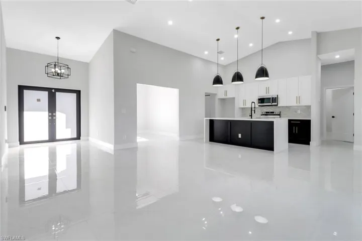 Kitchen featuring stainless steel microwave, light countertops, white cabinets, high vaulted ceiling, and a sink