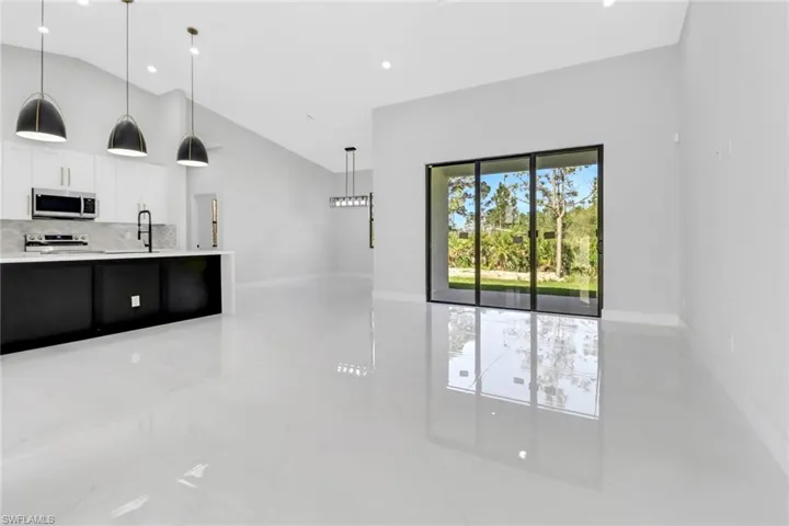 Kitchen with high vaulted ceiling, pendant lighting, stainless steel appliances, white cabinets, and light countertops