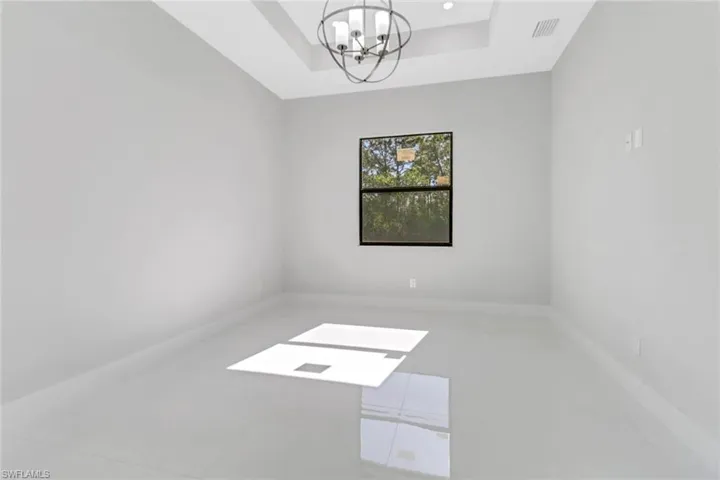 Empty room featuring a chandelier, visible vents, a raised ceiling, and baseboards
