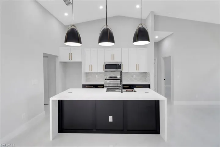 Kitchen with high vaulted ceiling, a sink, backsplash, stainless steel appliances, and white cabinets
