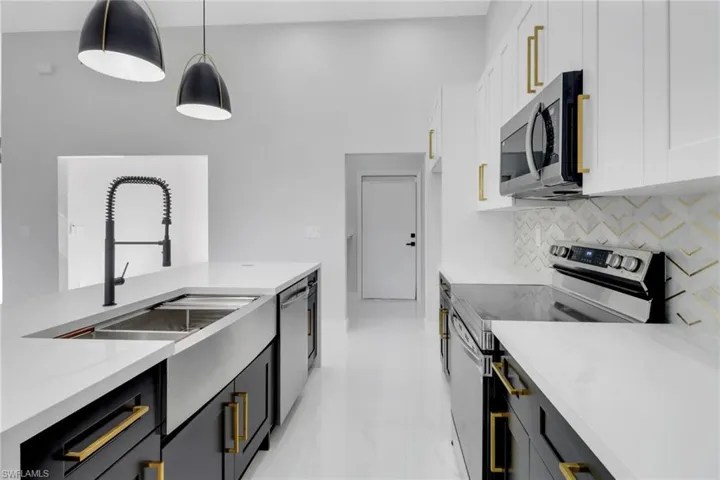 Kitchen with light stone countertops, stainless steel appliances, decorative backsplash, hanging light fixtures, and white cabinetry