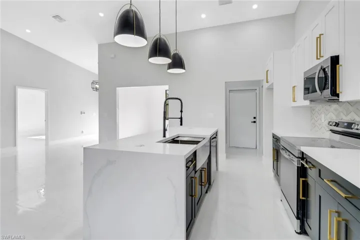 Kitchen featuring an island with sink, appliances with stainless steel finishes, marble finish floor, white cabinetry, and a sink