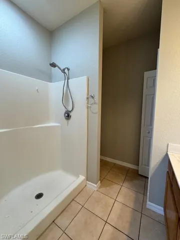Full bath with vanity, a stall shower, light tile patterned flooring, and a textured wall