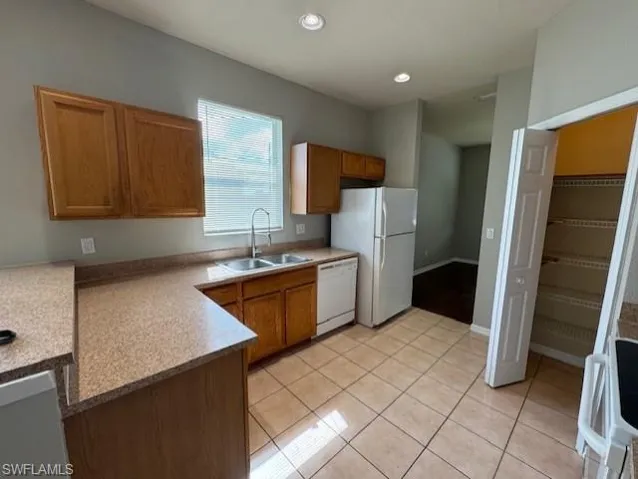 Kitchen featuring light tile patterned flooring, brown cabinetry, white appliances, recessed lighting, and a peninsula